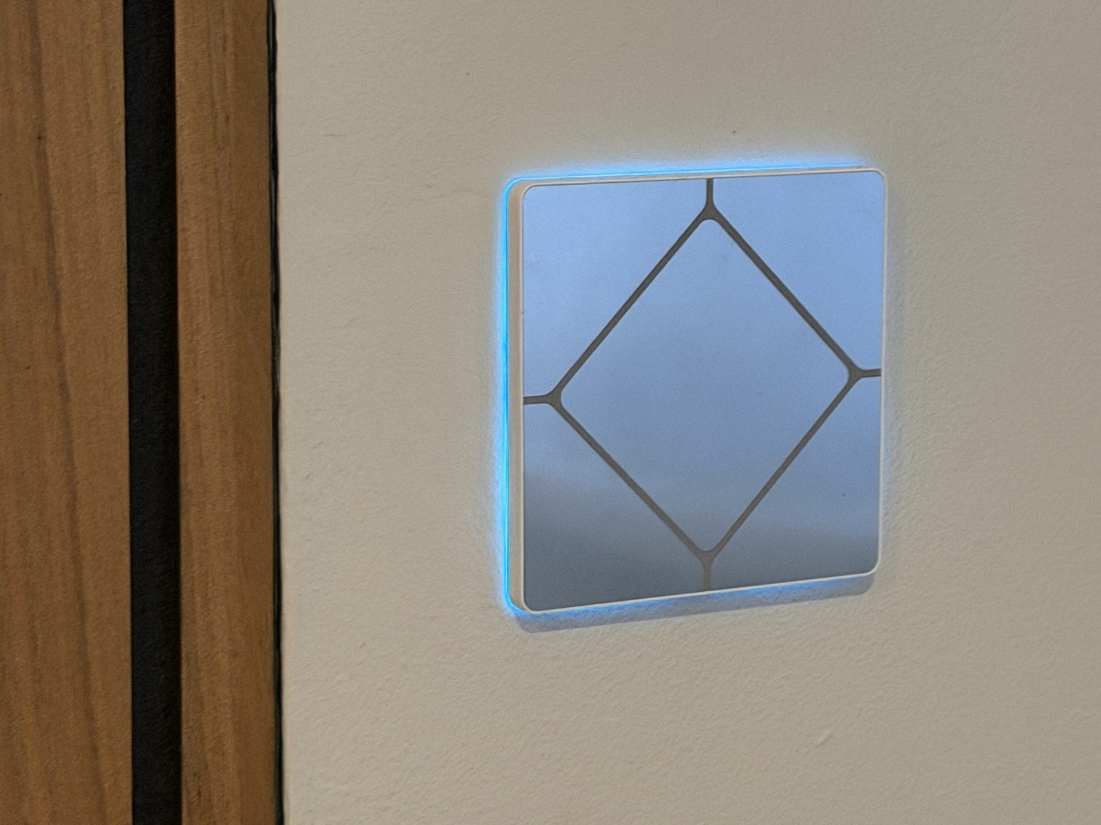 Faradite solid metal four-button KNX keypad with blue backlit buttons, mounted beside a wooden door frame