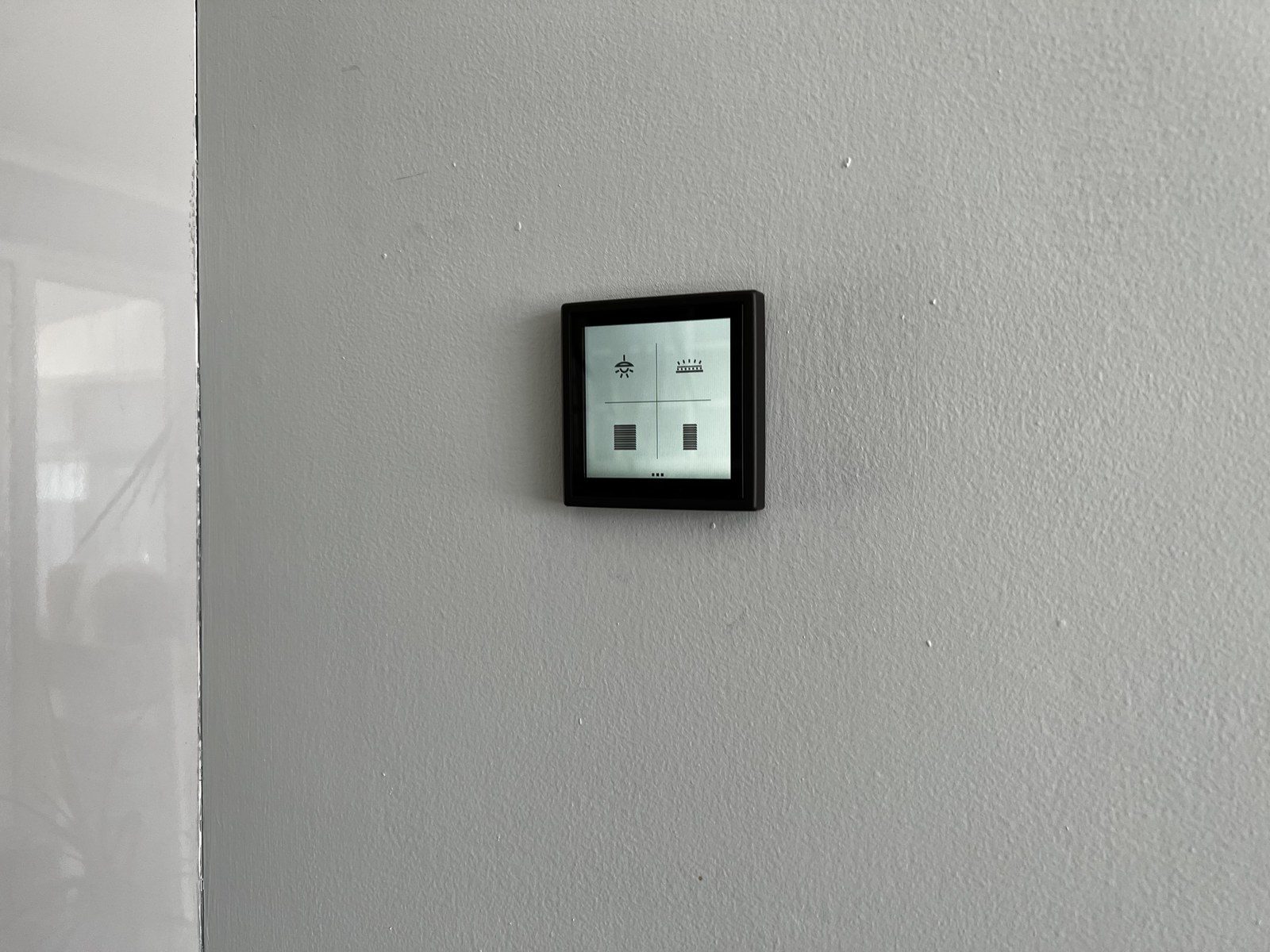 Black-framed touch display with lighting and blind controls on a grey wall